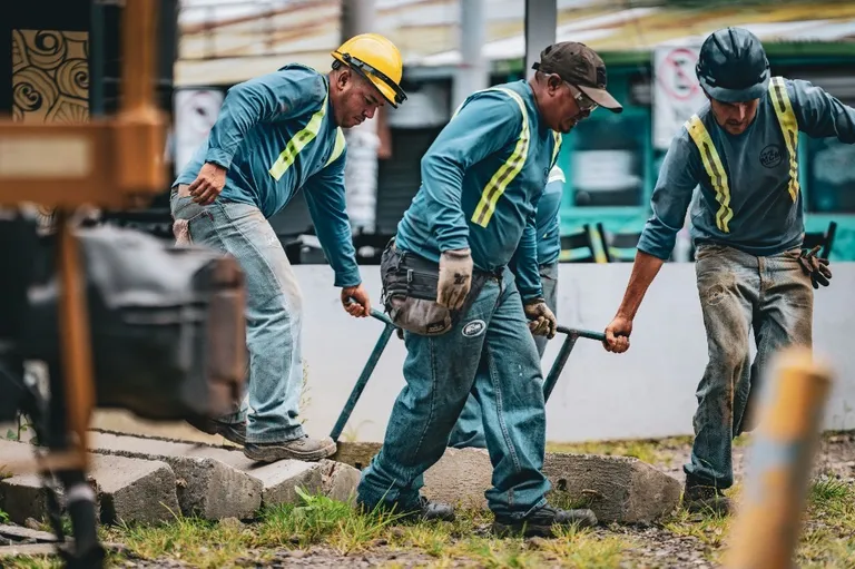 Equipe uniformizada em trabalho de campo, movendo blocos de concreto com alavanca